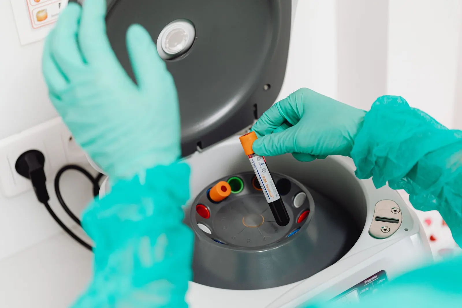 Gloved hands loading a blood sample tube into a laboratory centrifuge