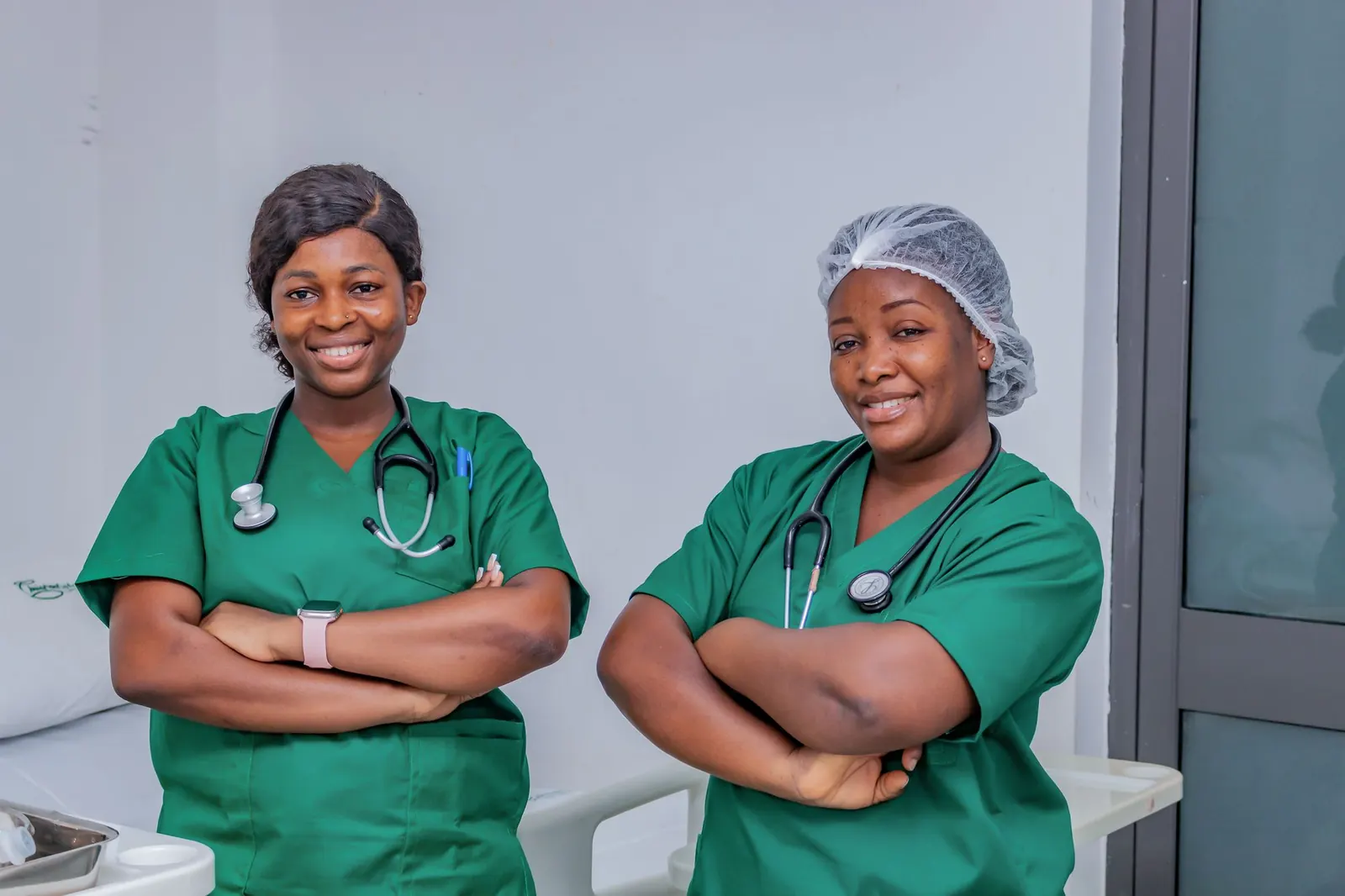 Two smiling nurses in green scrubs with stethoscopes in a clinic room